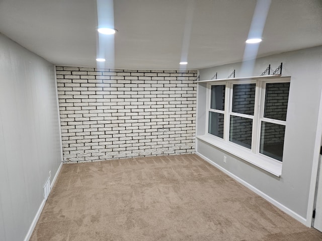 carpeted spare room featuring brick wall