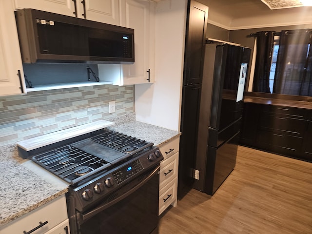 kitchen with white cabinets, decorative backsplash, light stone countertops, and black appliances