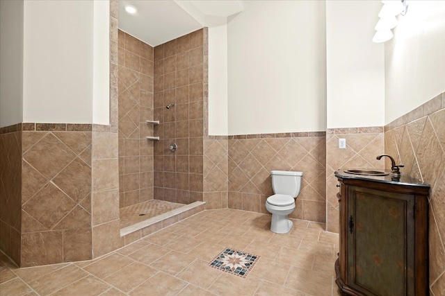 bathroom featuring tiled shower, vanity, toilet, and tile walls