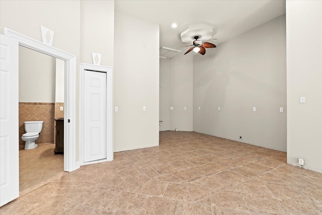 interior space featuring ceiling fan and tile walls