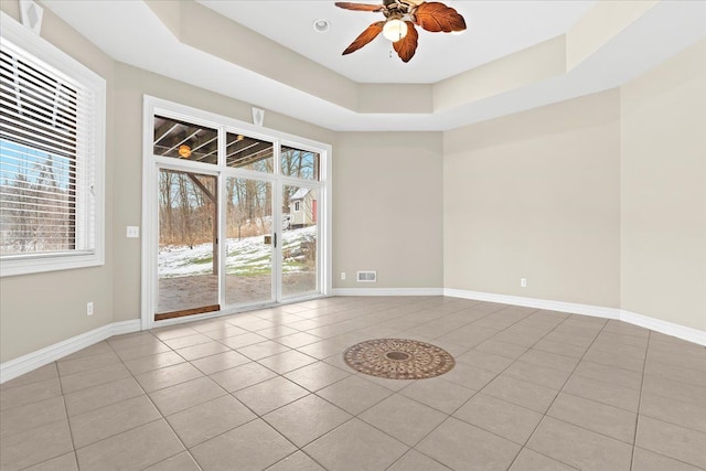 spare room with ceiling fan, light tile patterned flooring, a raised ceiling, and a wealth of natural light