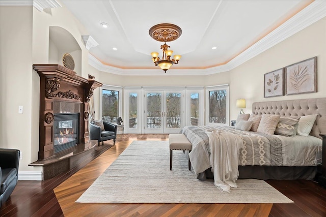 bedroom featuring a tray ceiling, access to exterior, hardwood / wood-style floors, and a tiled fireplace