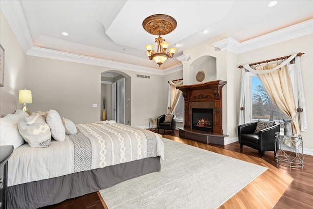 bedroom with hardwood / wood-style floors, a raised ceiling, a fireplace, and an inviting chandelier