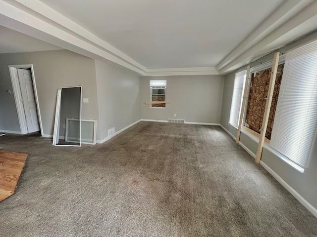 unfurnished room with carpet, baseboards, visible vents, and a raised ceiling