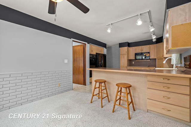 kitchen with sink, kitchen peninsula, a kitchen bar, light brown cabinetry, and black appliances