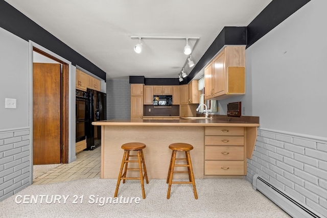 kitchen featuring light brown cabinets, a baseboard heating unit, black appliances, a kitchen bar, and kitchen peninsula