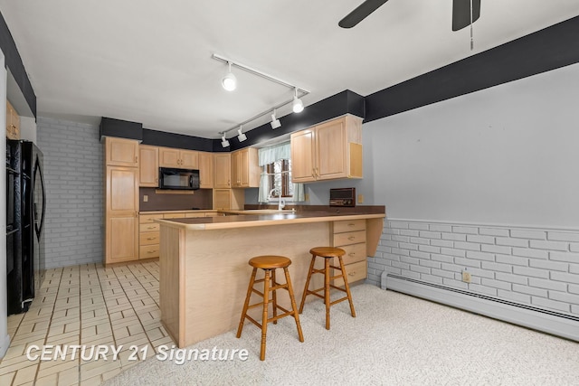 kitchen with light brown cabinets, baseboard heating, kitchen peninsula, a kitchen bar, and black appliances