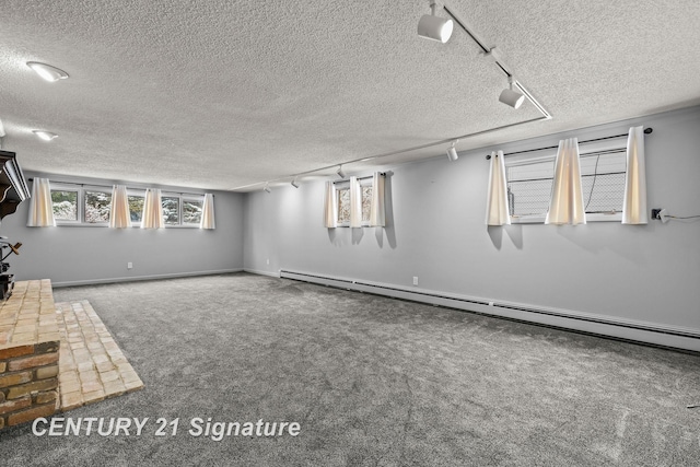 basement featuring carpet floors, rail lighting, a baseboard radiator, and a textured ceiling