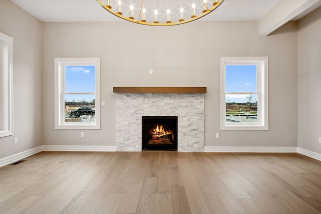 unfurnished living room with a healthy amount of sunlight, a stone fireplace, and light hardwood / wood-style flooring