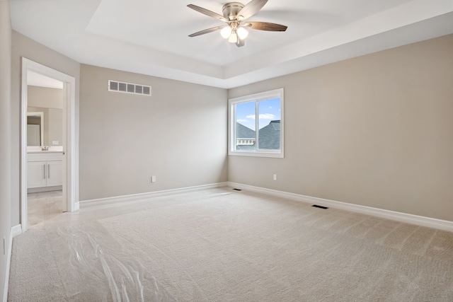 carpeted spare room featuring a raised ceiling and ceiling fan