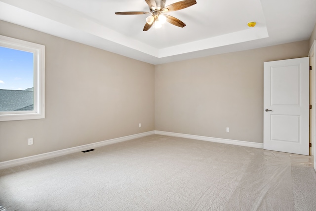 spare room with a tray ceiling, carpet floors, and ceiling fan