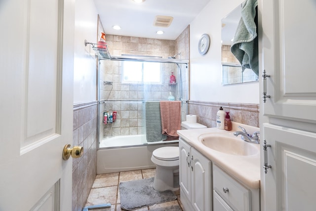 full bathroom with tile patterned flooring, shower / bath combination with glass door, tile walls, toilet, and vanity