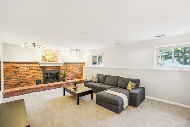 living room with a fireplace, visible vents, light carpet, track lighting, and baseboards