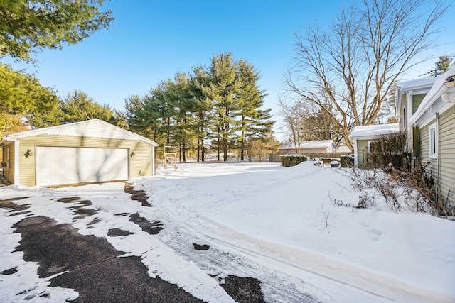 snowy yard with a garage, an outdoor structure, and fence