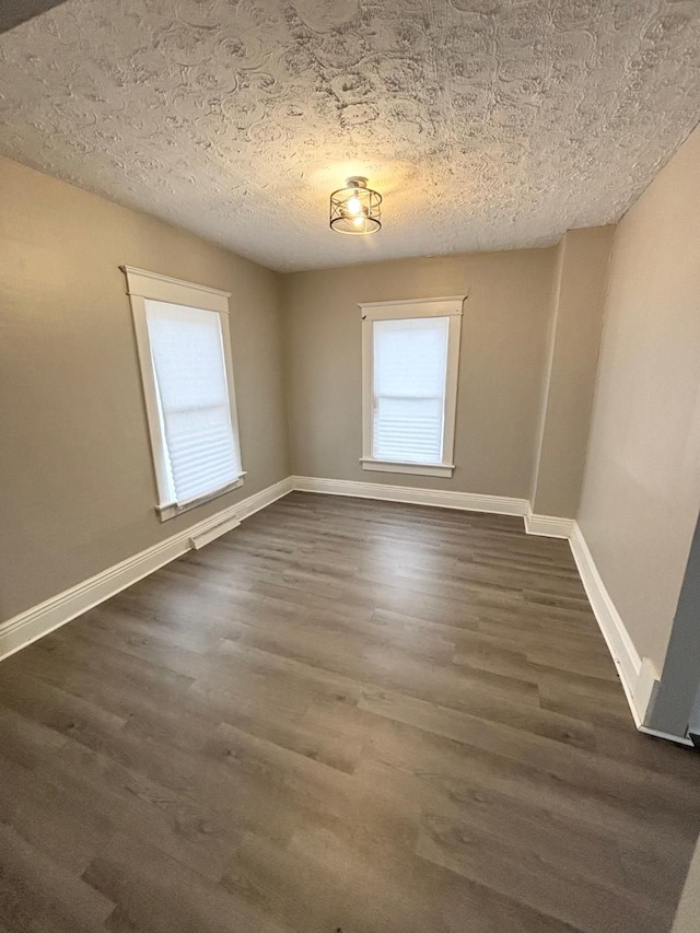 unfurnished room with dark wood finished floors, a textured ceiling, and baseboards