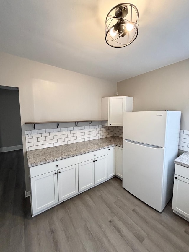 kitchen with light hardwood / wood-style flooring, backsplash, white refrigerator, light stone countertops, and white cabinets