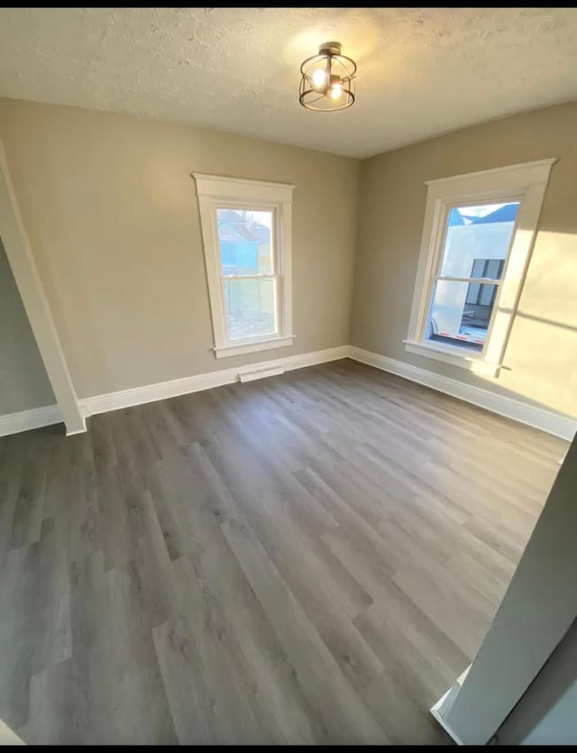 unfurnished dining area featuring a textured ceiling, wood finished floors, and baseboards