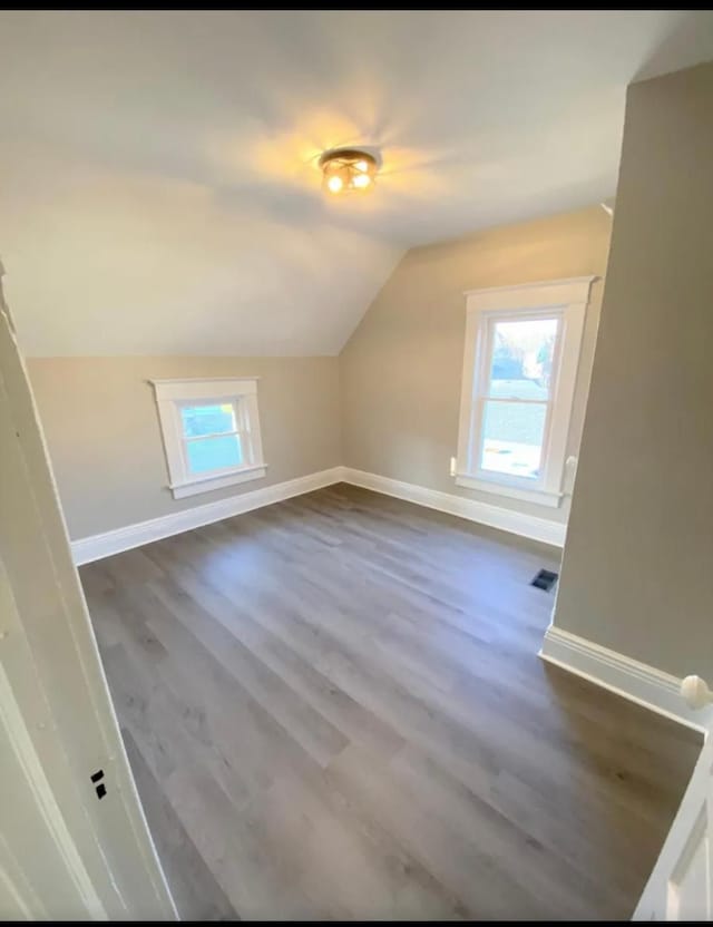 additional living space with dark wood-style floors, visible vents, baseboards, and vaulted ceiling