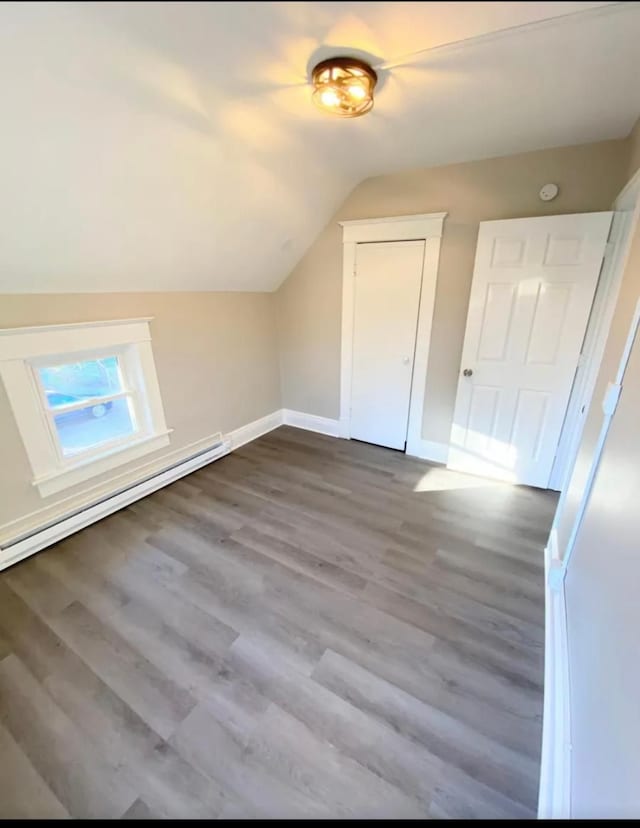 additional living space featuring baseboards, a baseboard heating unit, vaulted ceiling, and wood finished floors