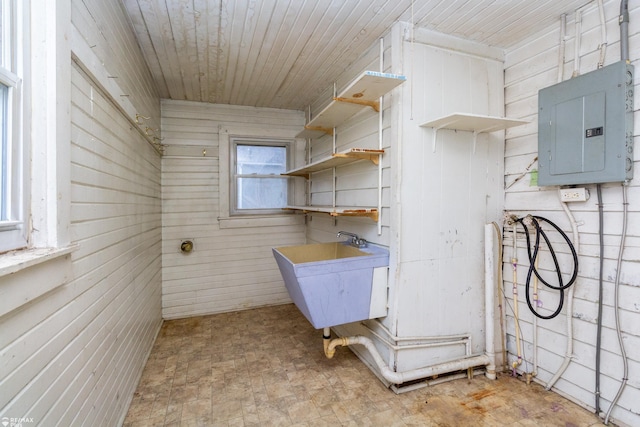 laundry area with wooden ceiling, electric panel, wooden walls, and sink