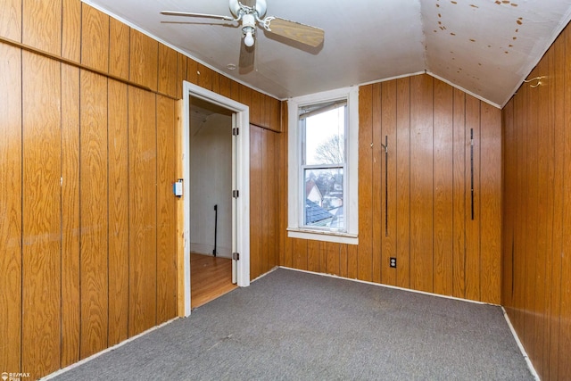 unfurnished bedroom featuring carpet, ceiling fan, lofted ceiling, and wood walls