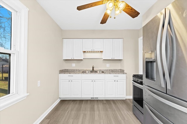 kitchen with light stone countertops, appliances with stainless steel finishes, white cabinetry, sink, and light hardwood / wood-style flooring