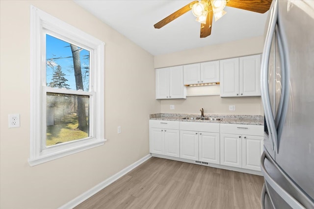 kitchen with light stone countertops, light hardwood / wood-style floors, sink, white cabinets, and stainless steel fridge