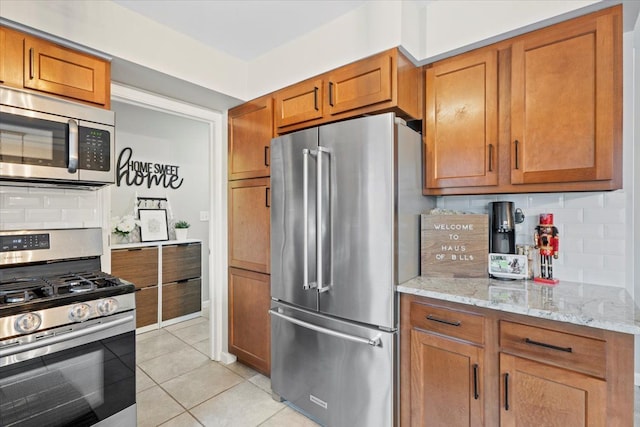 kitchen featuring decorative backsplash, light stone countertops, stainless steel appliances, and light tile patterned floors