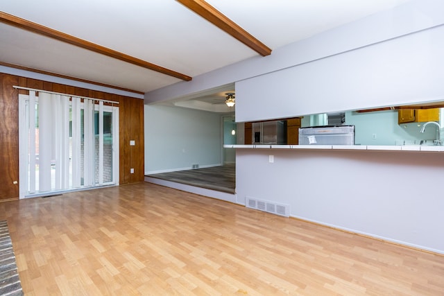 unfurnished living room with beamed ceiling, ceiling fan, sink, and light hardwood / wood-style flooring