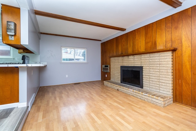 unfurnished living room with a wall mounted air conditioner, light hardwood / wood-style floors, ornamental molding, a fireplace, and beam ceiling