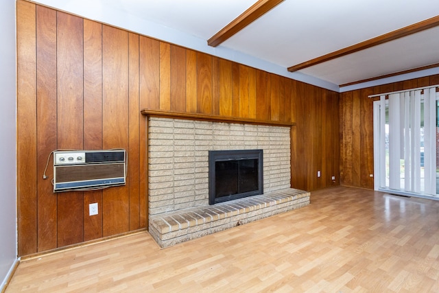 unfurnished living room featuring beamed ceiling, light hardwood / wood-style flooring, wooden walls, and a brick fireplace