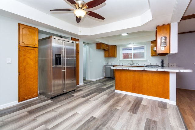 kitchen featuring light hardwood / wood-style flooring, ceiling fan, a tray ceiling, kitchen peninsula, and stainless steel appliances