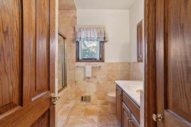 full bathroom with vanity, tile walls, bath / shower combo with glass door, and toilet