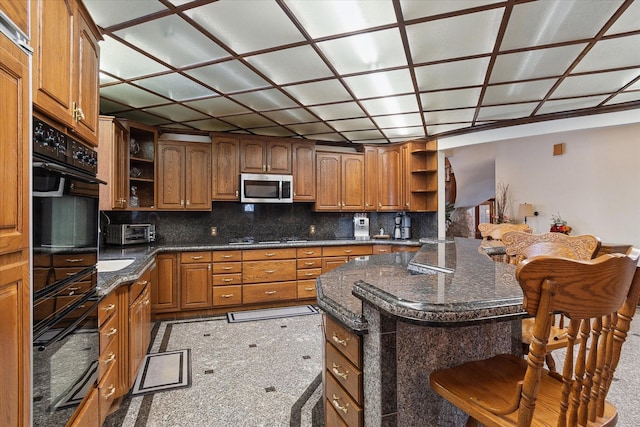 kitchen with a center island, dark stone counters, a breakfast bar, and black appliances