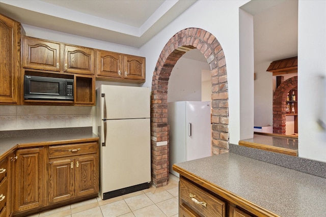 kitchen with white refrigerator, light tile patterned flooring, and backsplash