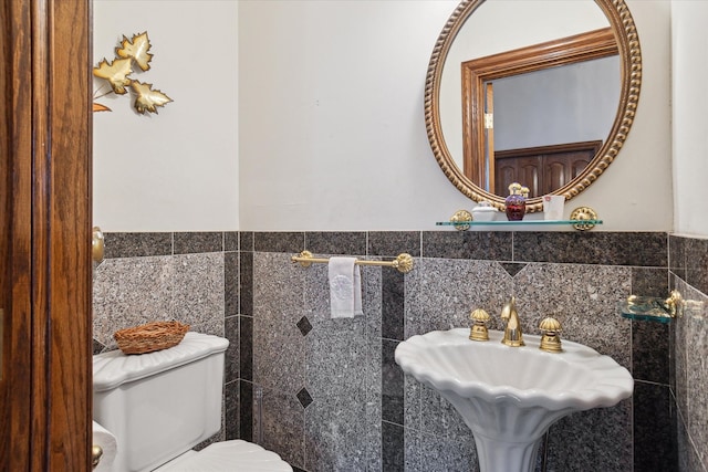 bathroom with toilet, sink, and tile walls