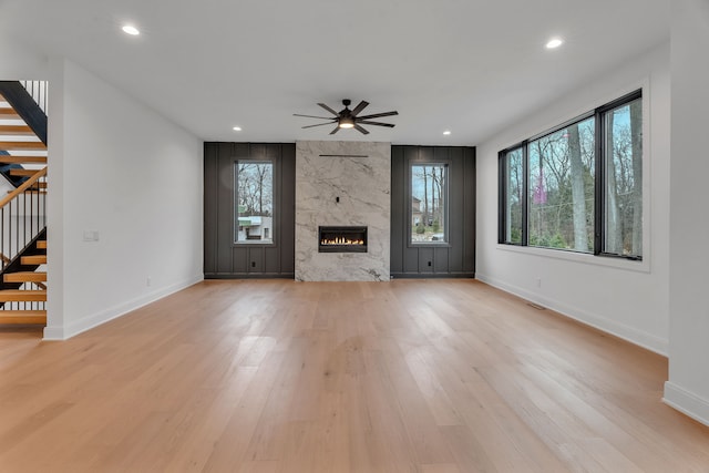 unfurnished living room featuring ceiling fan, light wood-type flooring, and a high end fireplace