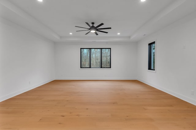 spare room featuring a raised ceiling, ceiling fan, and light wood-type flooring