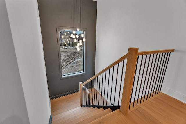 stairs with hardwood / wood-style floors and an inviting chandelier