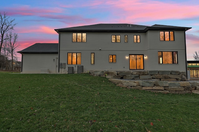 back house at dusk with a lawn and central AC unit