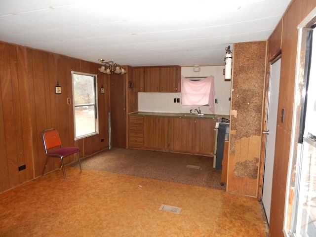 kitchen featuring carpet flooring, sink, an inviting chandelier, wood walls, and range