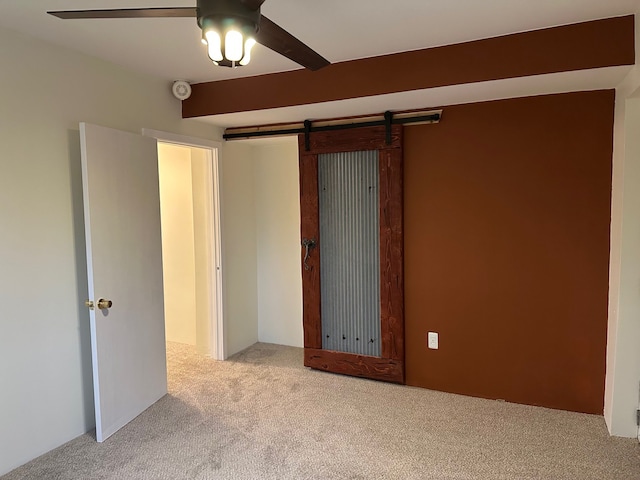 unfurnished bedroom with light colored carpet, a barn door, and ceiling fan