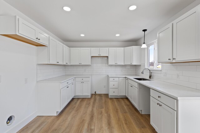 kitchen featuring pendant lighting, sink, light hardwood / wood-style flooring, tasteful backsplash, and white cabinetry