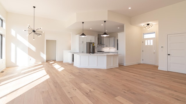 kitchen featuring a center island with sink, wall chimney range hood, hanging light fixtures, stainless steel refrigerator, and a chandelier