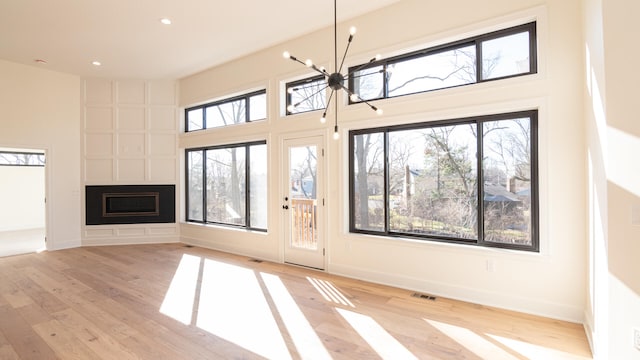 332 Arbor Ln, Saline, MI 48176 - unfurnished living room with a chandelier, light wood-style floors, recessed lighting, a fireplace, and a towering ceiling