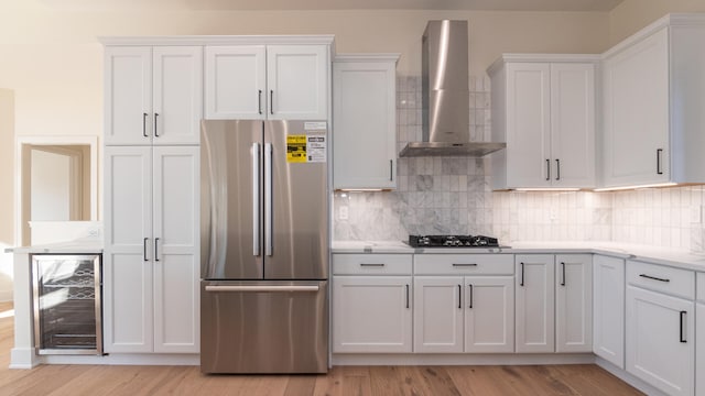 kitchen featuring wall chimney range hood, decorative backsplash, white cabinetry, stainless steel refrigerator, and gas cooktop