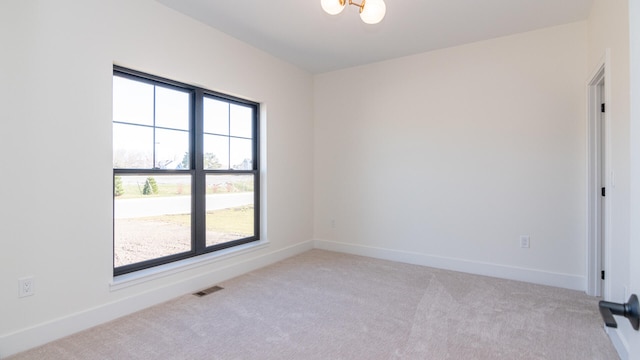 empty room featuring a healthy amount of sunlight, light colored carpet, and a chandelier