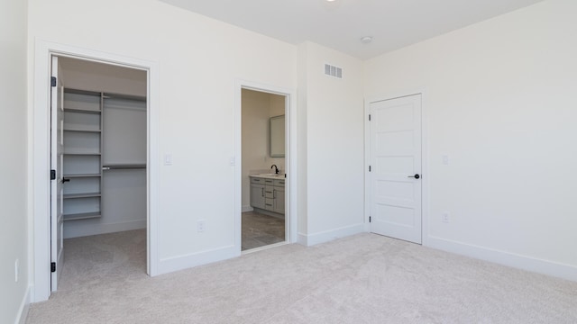 unfurnished bedroom featuring a spacious closet, light carpet, connected bathroom, and a closet