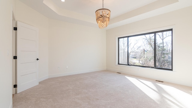 spare room featuring a notable chandelier, plenty of natural light, light carpet, and a tray ceiling