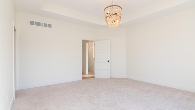 carpeted spare room with an inviting chandelier and a raised ceiling